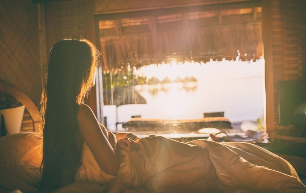 Woman in bed looking at lagoon Bora Bora