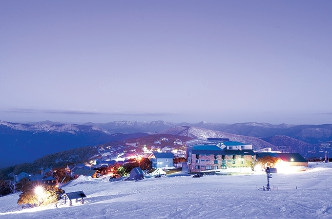 Aerial view of the ski resort at Mt Buller with snowy mountains in the background and lit buldings during nighttime