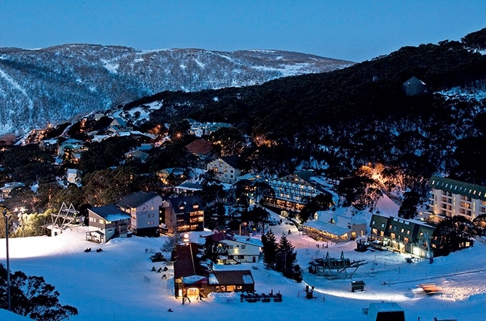 Aerial view of the snowy Ski Resort at Falls Creek during nighttime with building lights and mountain ranges in the background