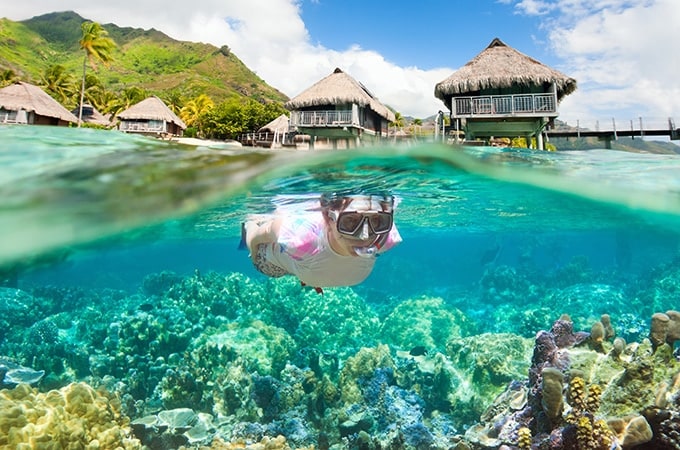 Woman snorkeling on a beach in Bora Bora with overwater bungalows on the background