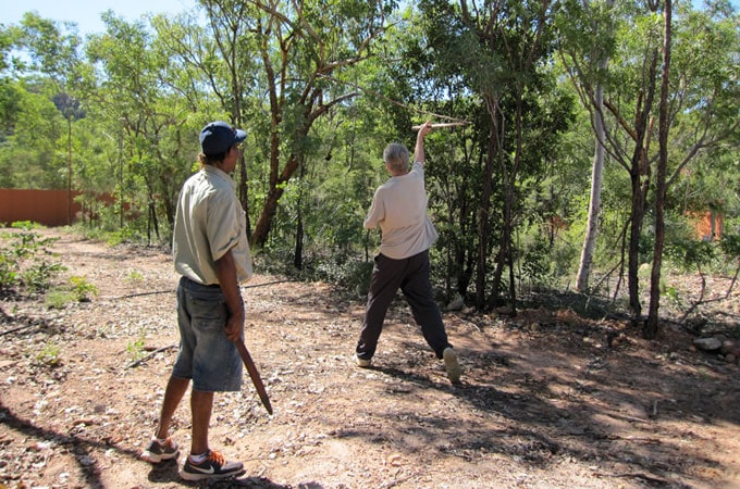 A couple of men learning how to use a whip in the middle of the woods at Cicada Lodge