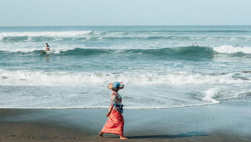 A local woman makes her morning offerings along Batu Balong beach, as surfers carve up the famous Canggu waves.