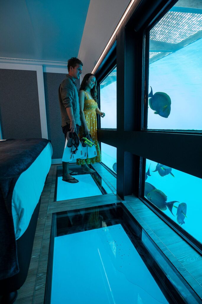 A couple admiring the view from their underwater room with fishes swimming outside the window at the Whitsundays