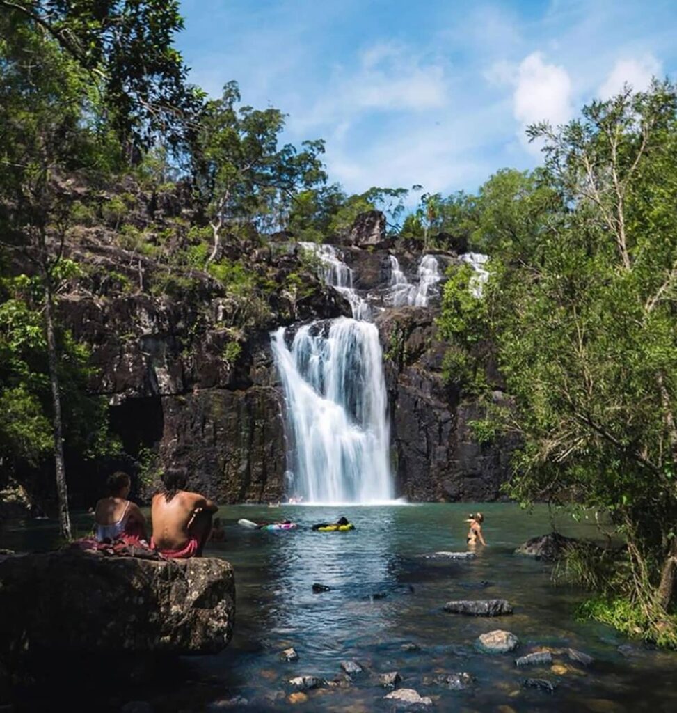 Tourists taking a dip on a plunge pool at the Whitsundays with a waterfall in the background and surrounding lush greeneries and trees