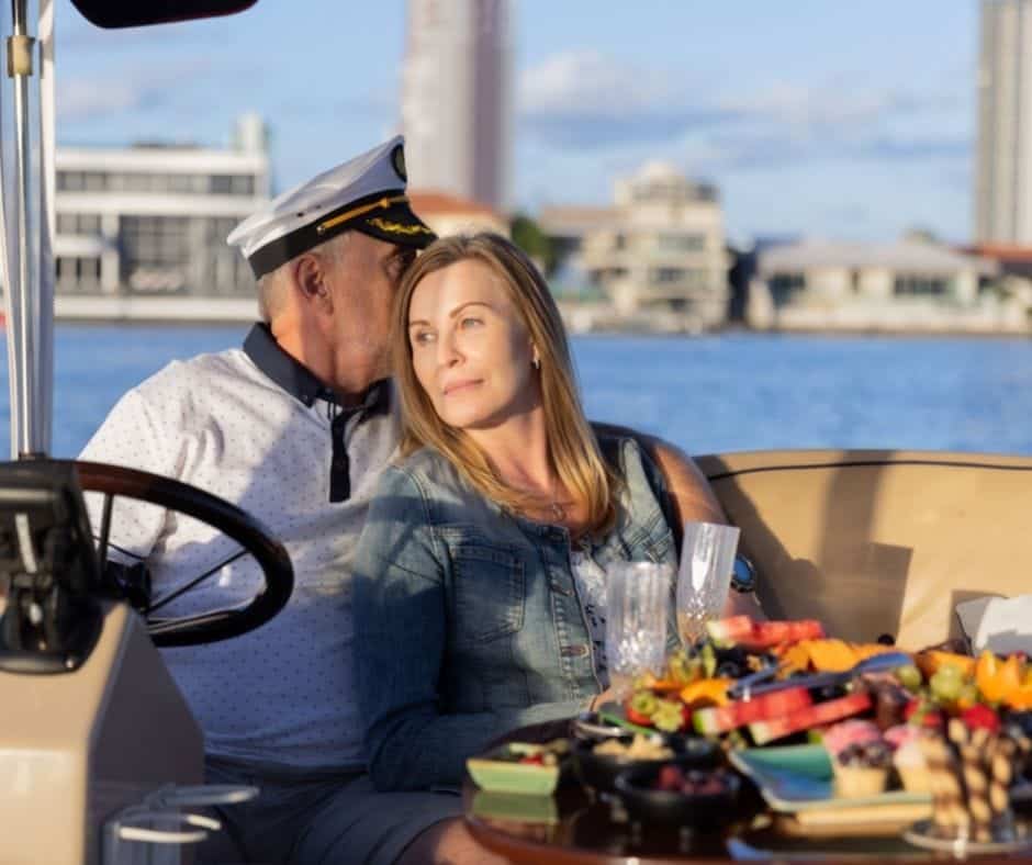 Romantic couple sitting on a cruising boat with food on the table and buildings on the background with Duffy Downunder's Boats