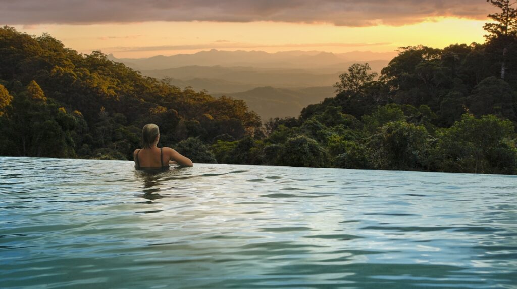 Woman enjoying the view of the surrounding forest with lush greeneries and trees on an infinity pool at O'Reilly's in The Gold Coast Hinterland during sunset