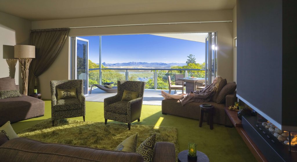Woman sitting and lounging at O'Reilly's Rainforest Retreat Canopy Room with indoor-outdoor space and views of the surrounding forests, lakes, and mountains
