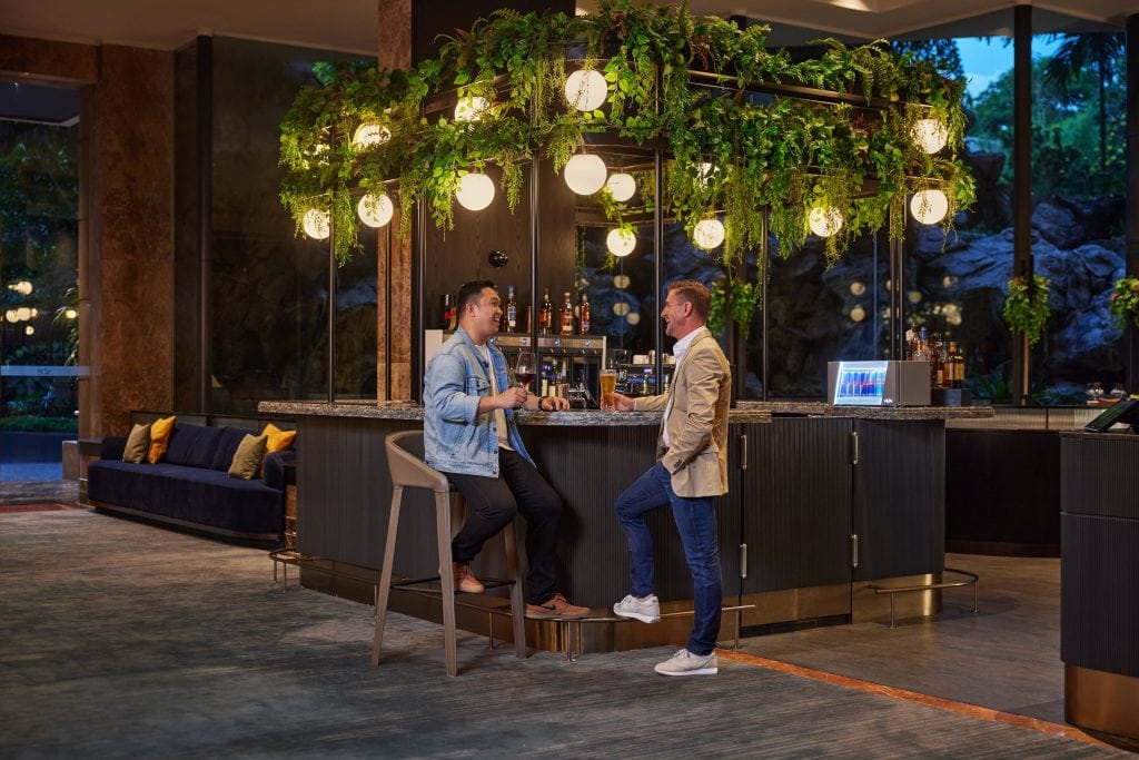 A couple of friends or two men drinking and taking at the orchard lobby bar with counters, seats, tables, and floor-to-ceiling glass windows or doors at the Vibe Hotel in Singapore
