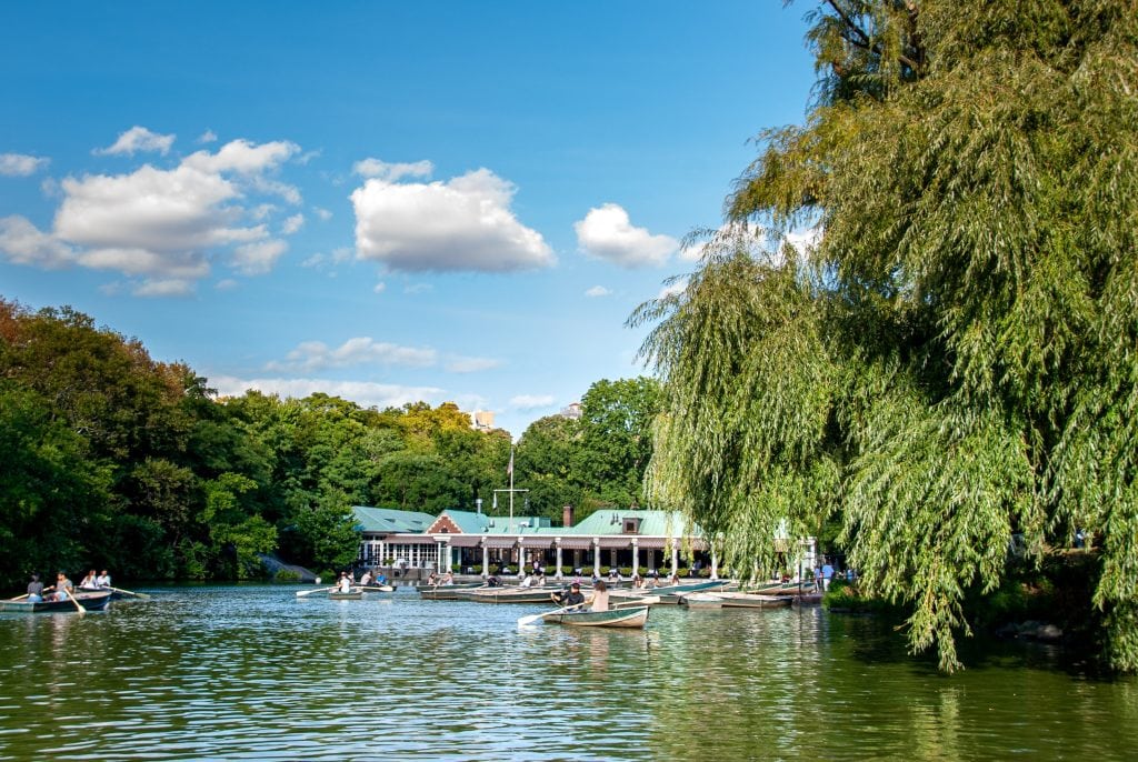 Boathouse Restaurant on a lake in Central Park, New York with paddle boats on the foreground and lush greeneries and trees on the background