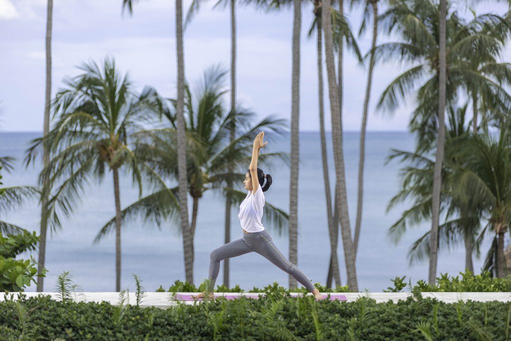Woman-doing-yoga-or-stretching-exercises-with-palm-trees-and-beach-on-the-background-in-Banyan-Tree-Koh-Samui
